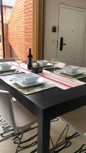 Et spisebord dækket med hvide tallerkener, skåle og bestik, samt en vinflaske og en stribet dug.