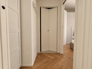 A hallway with a wooden floor leading to a white door. - New Listing (Milano)