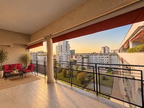 A balcony with a red sofa, a small table, and potted plants. - New Listing (Milano)