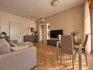 A modern living room with a sofa, dining table, chairs, and a TV. - New Listing (Milano)