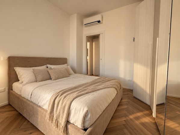 A bedroom with a bed, a wardrobe, and an air conditioning unit. - New Listing (Milano)