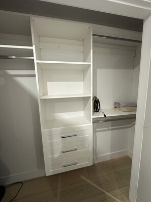 Un dressing accessible sans porte, avec des étagères ouvertes, une serviette pliée sur l’étagère du haut et un câble d’alimentation sur le côté droit.