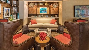 Een gezellige woonkamer met een bank, twee fauteuils, een salontafel en een boekenplank vol met allerlei spullen.