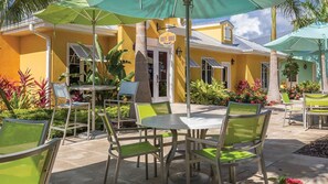 Een terras buiten met tafels en stoelen, een geel gebouw met een bord waarop