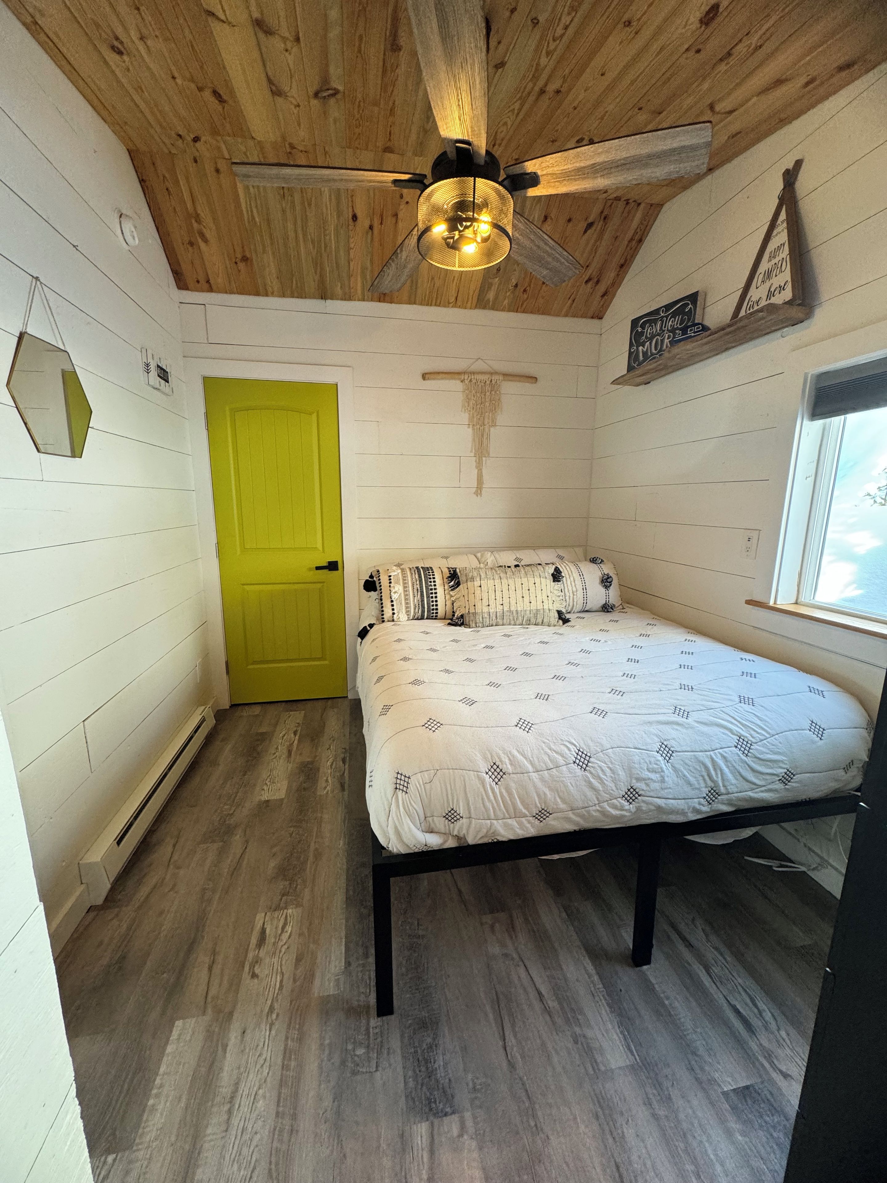 A bedroom with a bed, a ceiling fan, a wooden door, and a window.