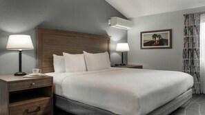 Ett hotellrum med en stor säng, två sängbord med lampor, en väggmonterad luftkonditioneringsanläggning och en inramad tavla på väggen.