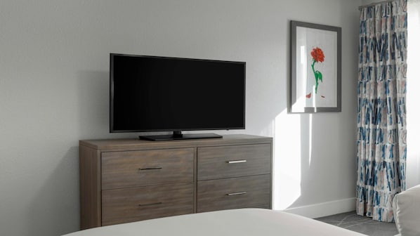 Ein modernes Schlafzimmer mit einem Flachbildfernseher auf einer Holzkommode, einem gerahmten Bild an der Wand und einem gemusterten Vorhang.