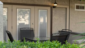 Eine Terrasse mit einem Glastisch und Stühlen, einer Tür mit Jalousien und einer Wandleuchte.