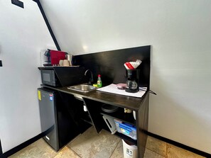 Eine kompakte Küchenzeile mit Mikrowelle, Kaffeemaschine und kleinem Kühlschrank.