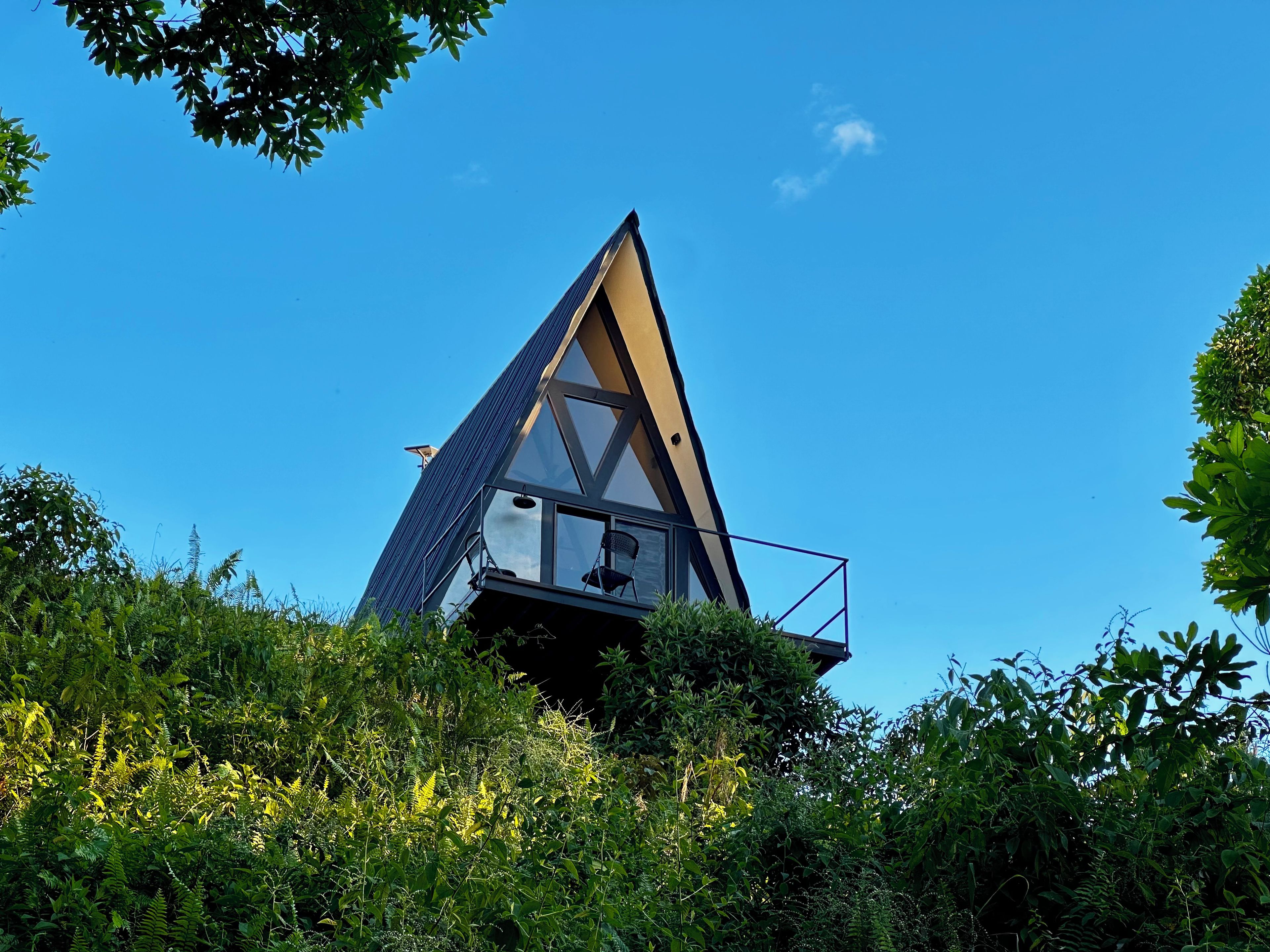 En moderne, trekantet bygning med balkon, omgivet af frodig vegetation.