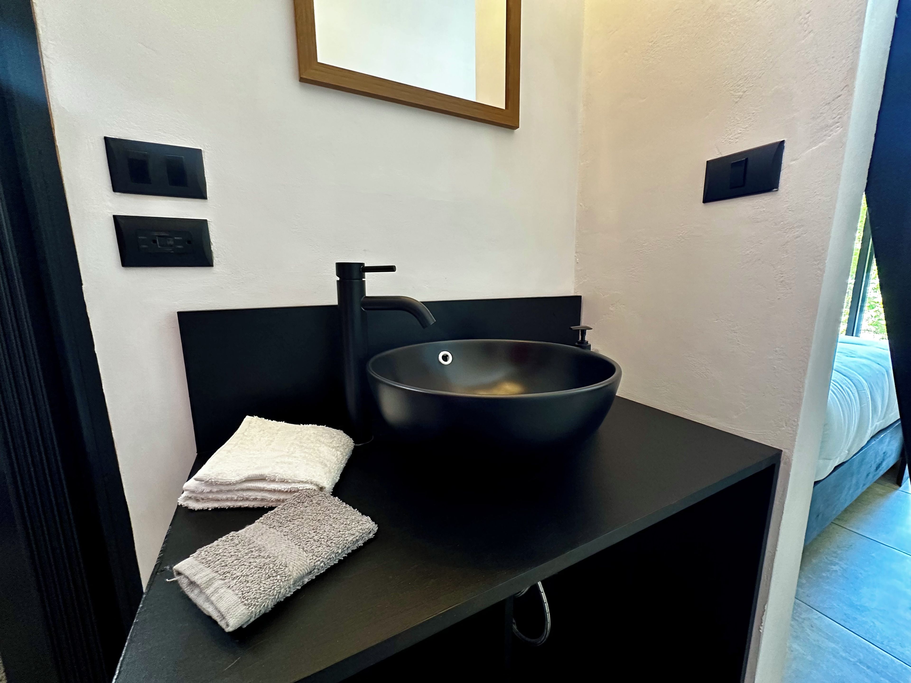 Un baño moderno con un lavamanos negro, dos toallas y un espejo enmarcado en la pared.