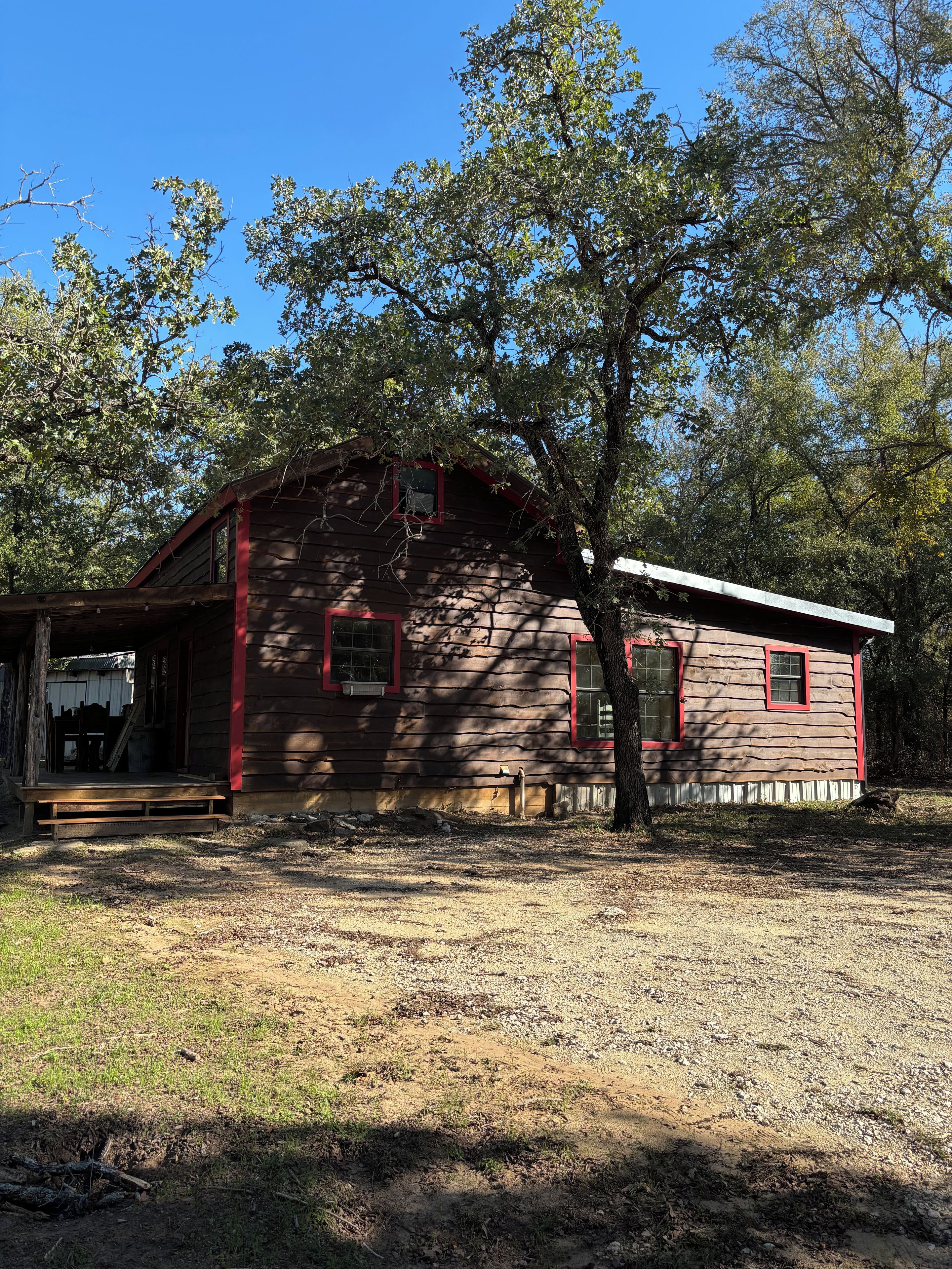 A rustic wooden cabin with a porch, surrounded by trees and a clear sky.