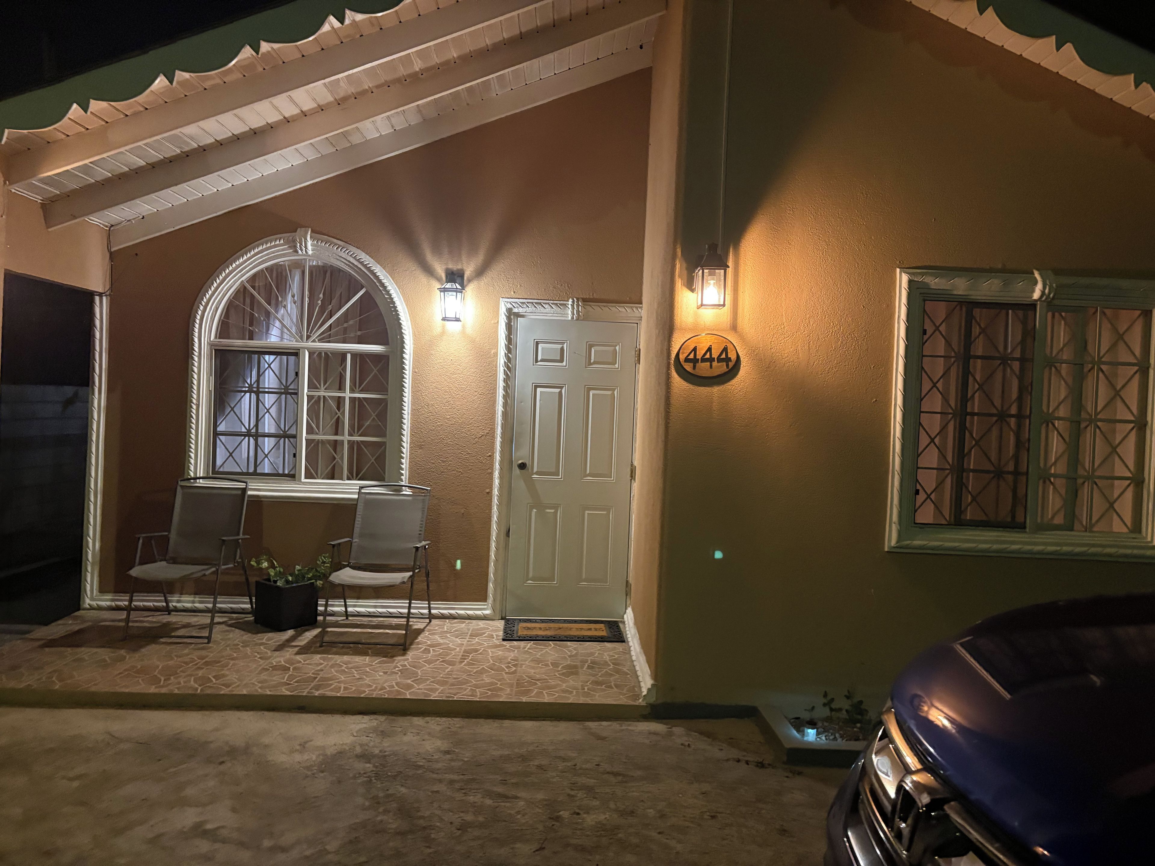 A house with a covered porch, a door with a number sign, and a car parked in the driveway.