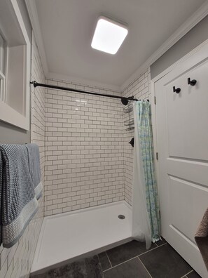 Un baño con paredes de azulejos blancos, una zona de ducha, un perchero y una puerta con una toalla colgada.