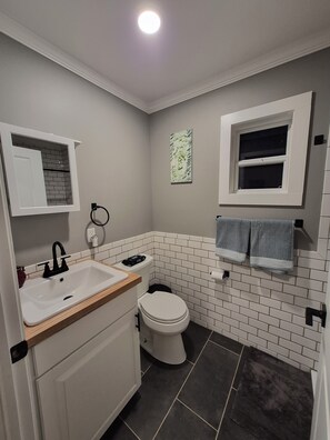 Un baño con lavamanos blanco, inodoro, toallero y ventana.