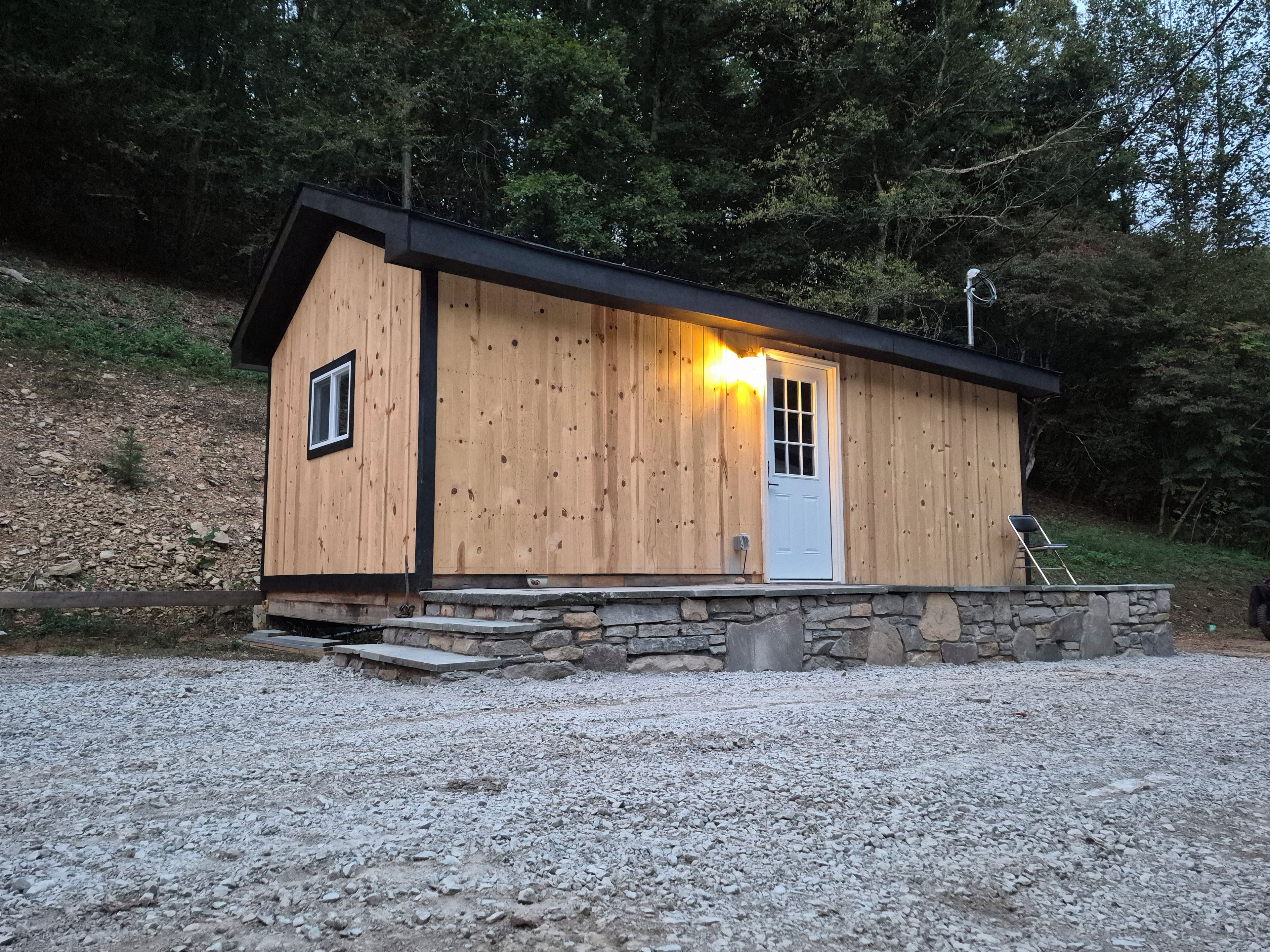 Una cabana de fusta amb fonaments de pedra, una porta i una finestra.