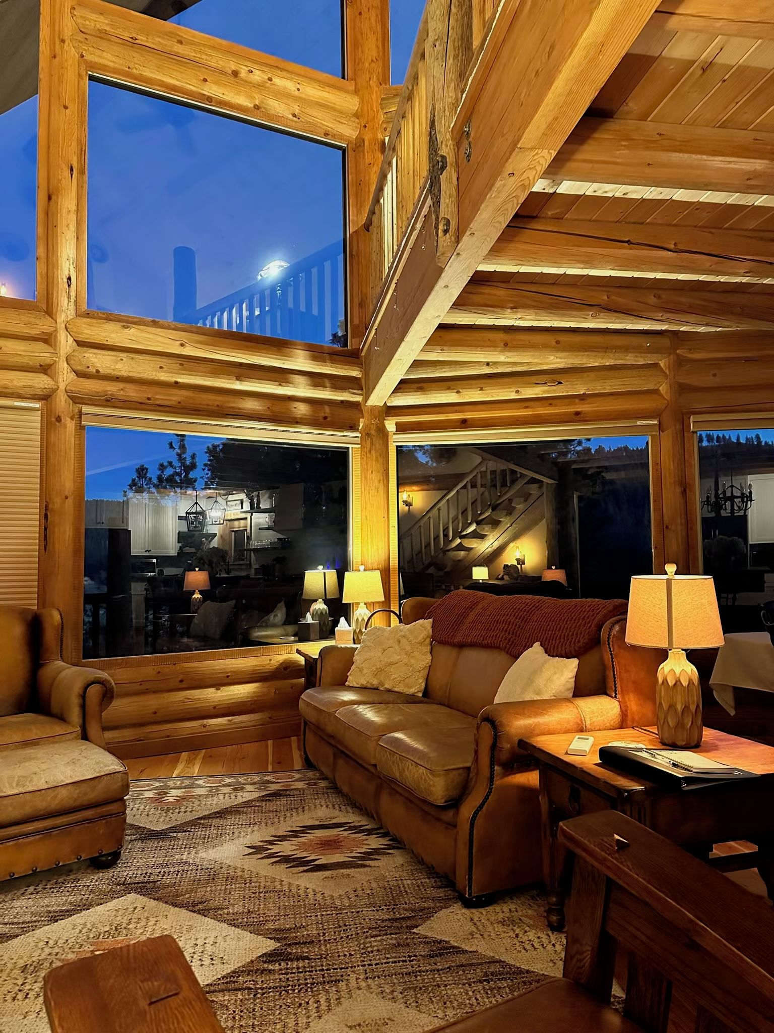 A log cabin interior with a large window, a staircase, and a cozy seating area.