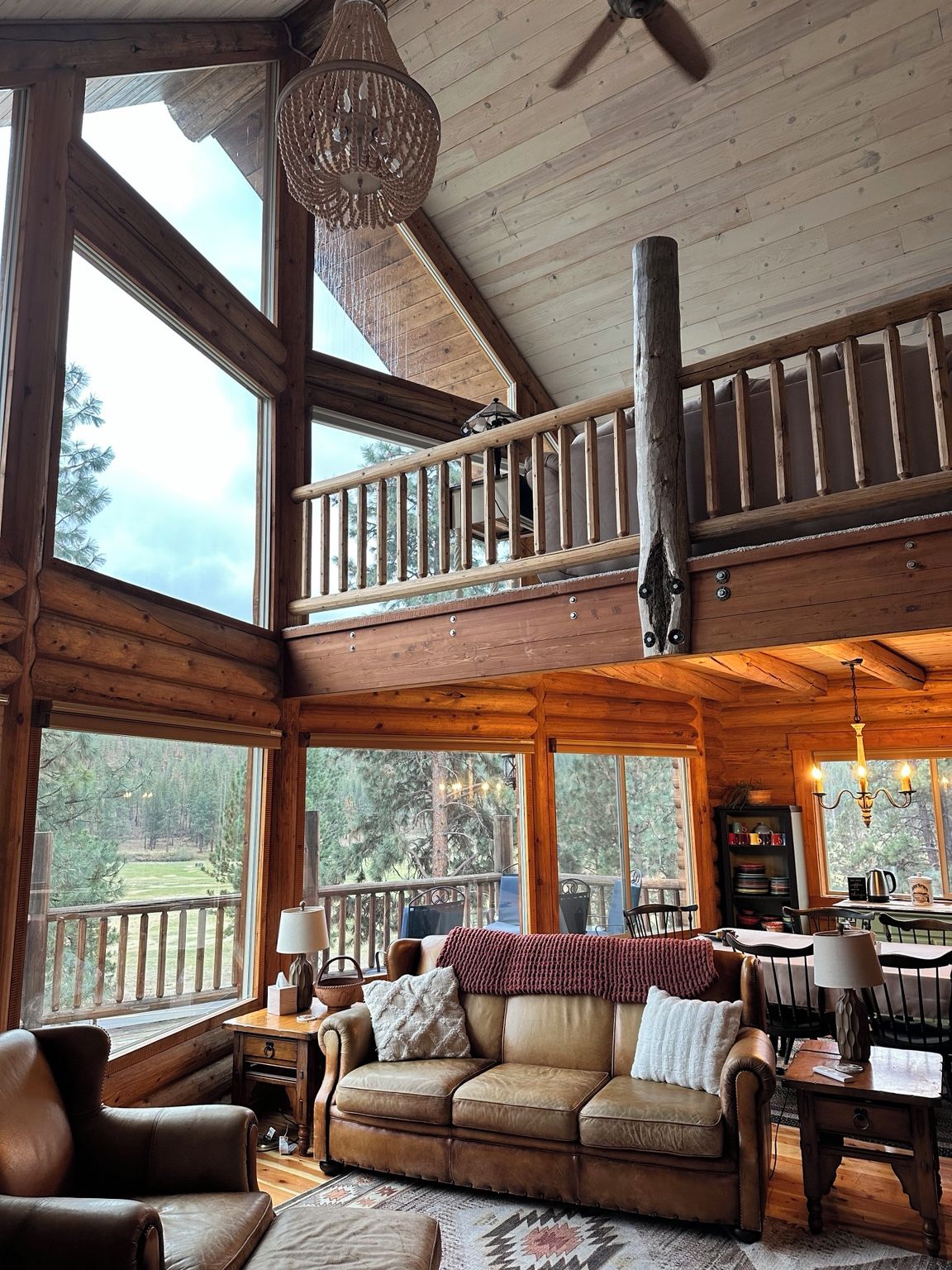 A spacious cabin with a loft bedroom, large windows, a dining area, and a cozy living room with leather furniture.
