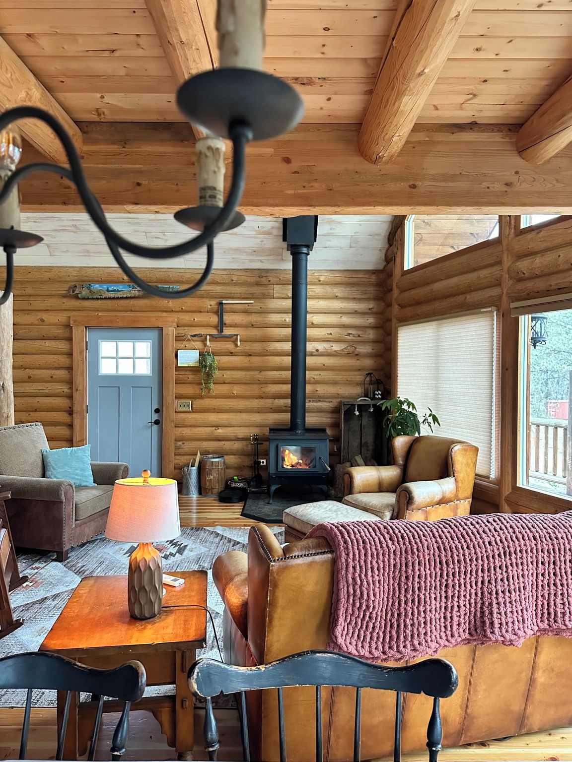A log cabin interior with a fireplace, wooden walls, a sofa, and a dining area.