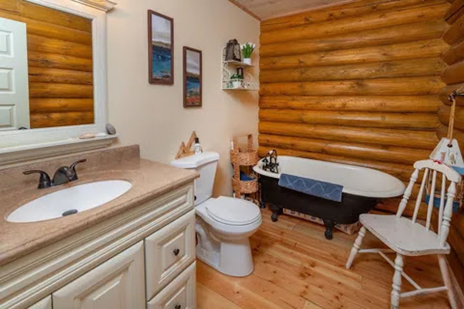 Une salle de bain rustique, aménagée dans une cabane en rondins, avec un lavabo, des toilettes, une baignoire et une chaise.