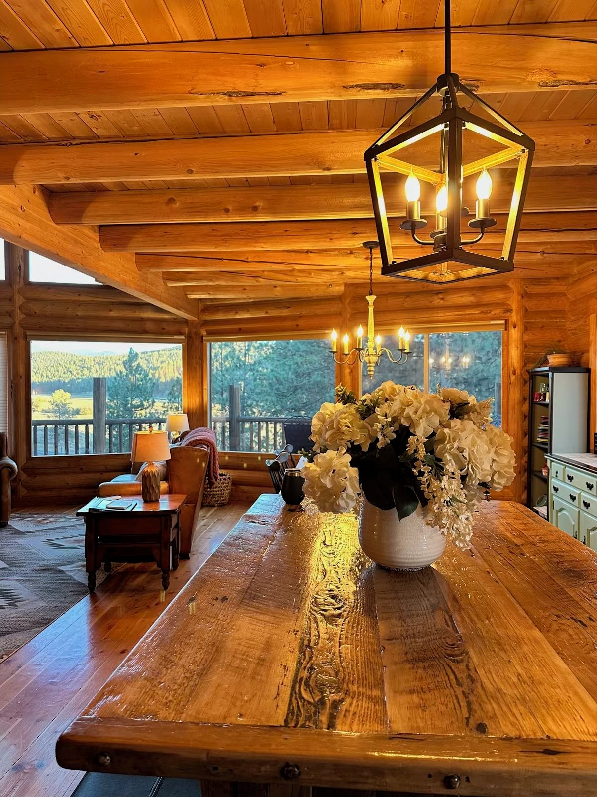 A wooden interior with a large table, a chandelier, and a vase of flowers.