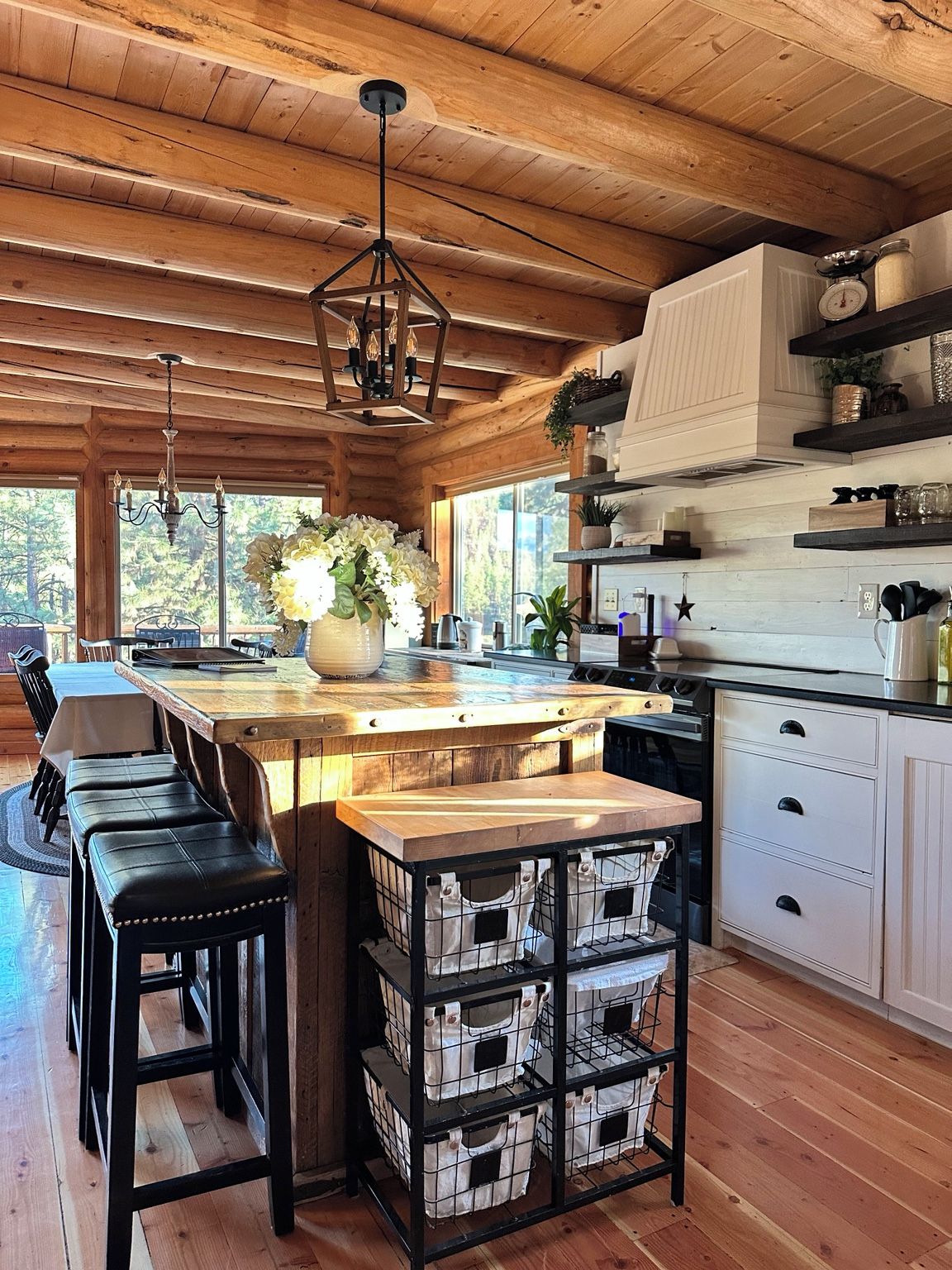 A kitchen with wooden beams, a central island, bar stools, and a hanging light fixture.