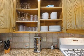 Una cocina con armarios de madera, estufa a gas, especias y diferentes utensilios de cocina.