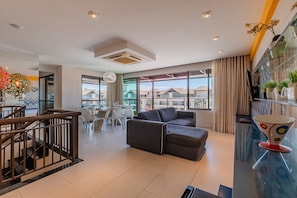 Uma sala de estar moderna com sofá, área de jantar e grandes janelas com vista para os edifícios ao redor.