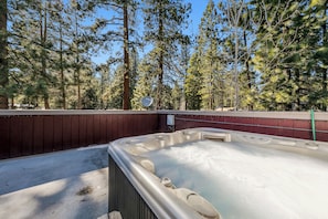 A hot tub in a wooded area with a wooden deck and a satellite dish.