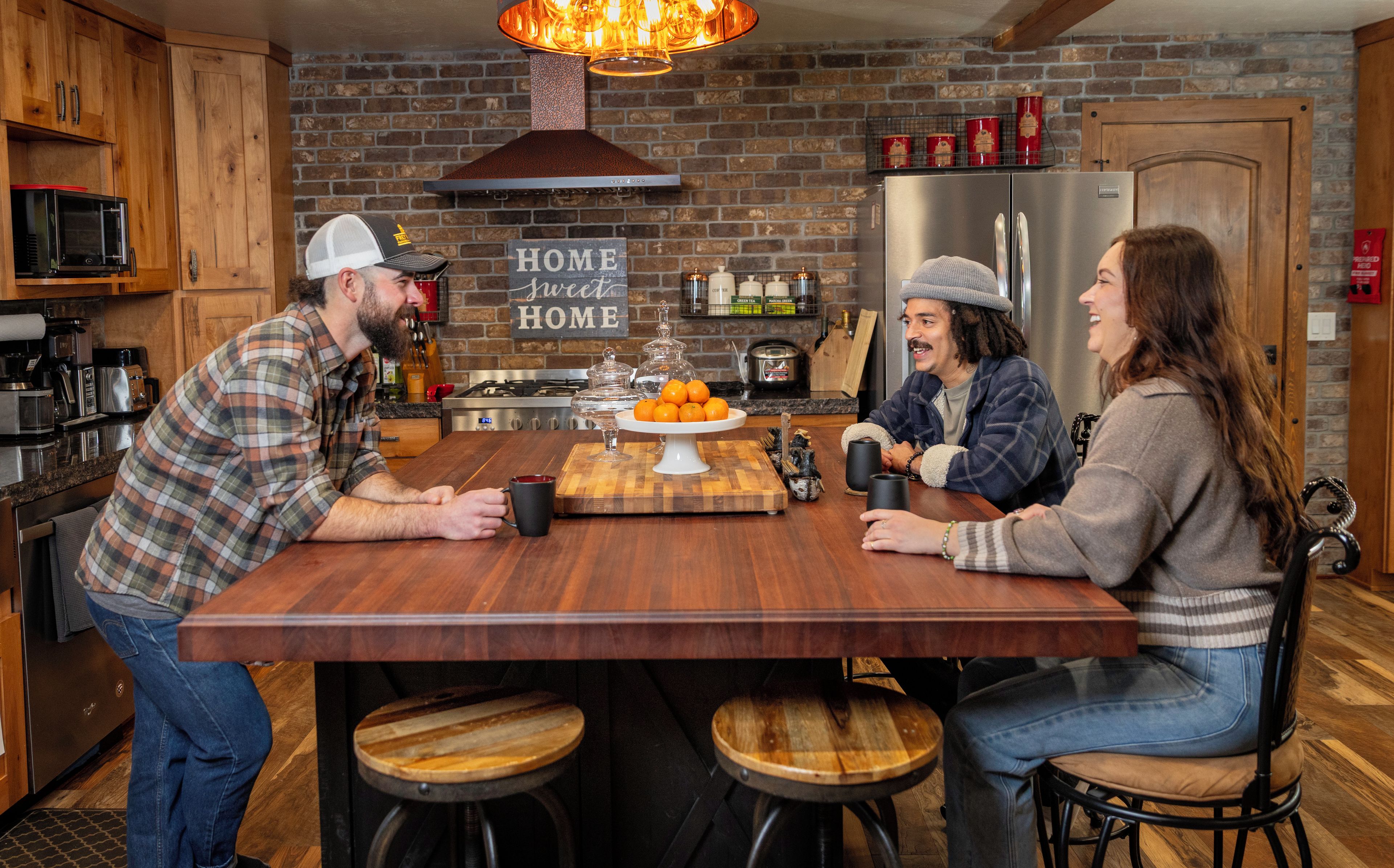 A kitchen with wooden cabinets, a brick wall, a stainless steel refrigerator, and a sign that reads 'HOME sweet HOME'.