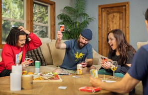 A group of people playing a card game around a table with snacks and drinks.