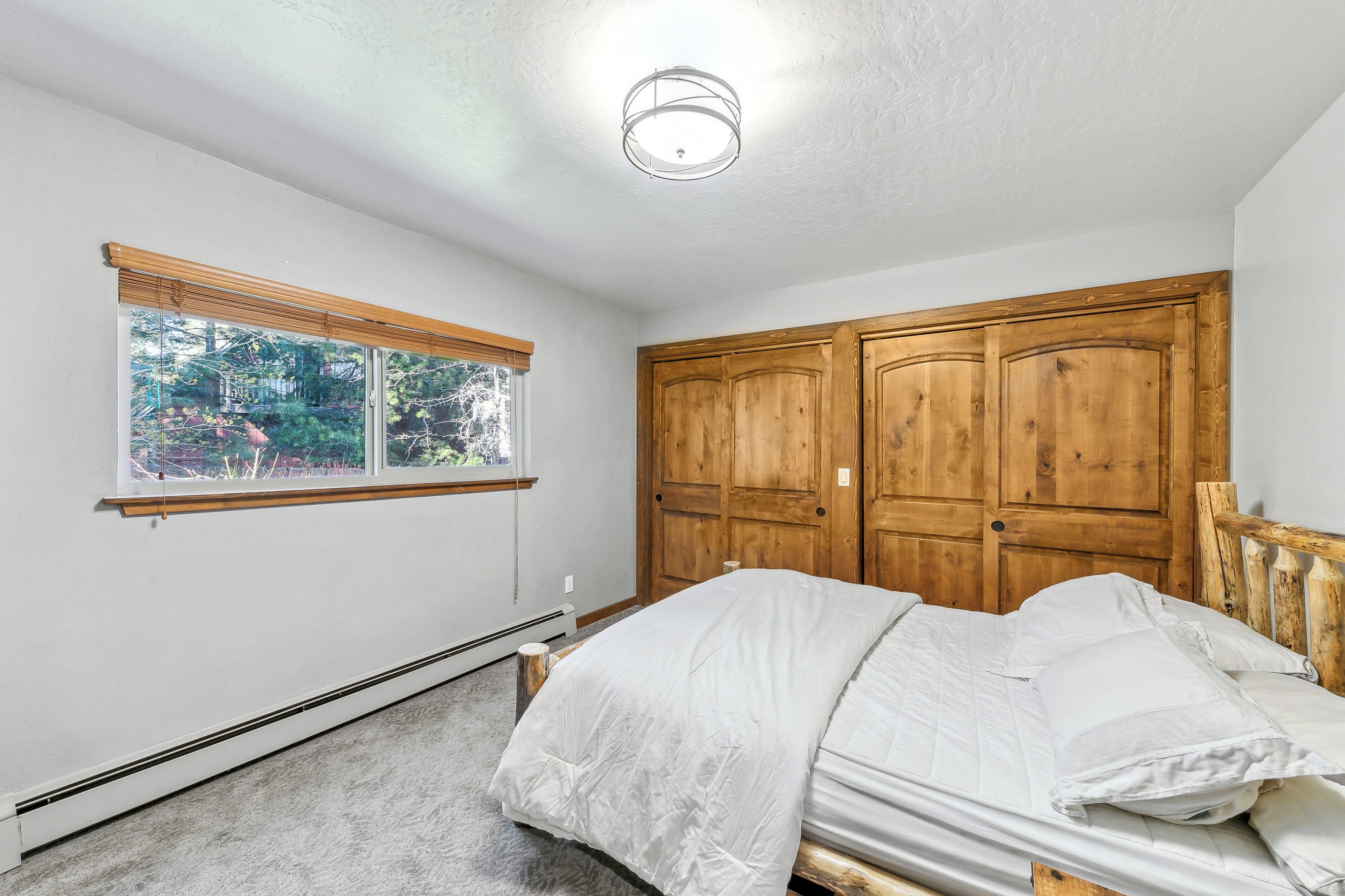 Ein Schlafzimmer mit einem Bett, einem Fenster mit Jalousien, einer Deckenleuchte und Holzschränken.