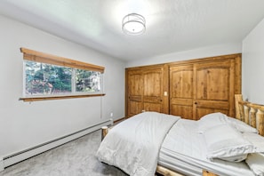 Quarto com cama, janela com persianas, luminária no teto e armários de madeira.