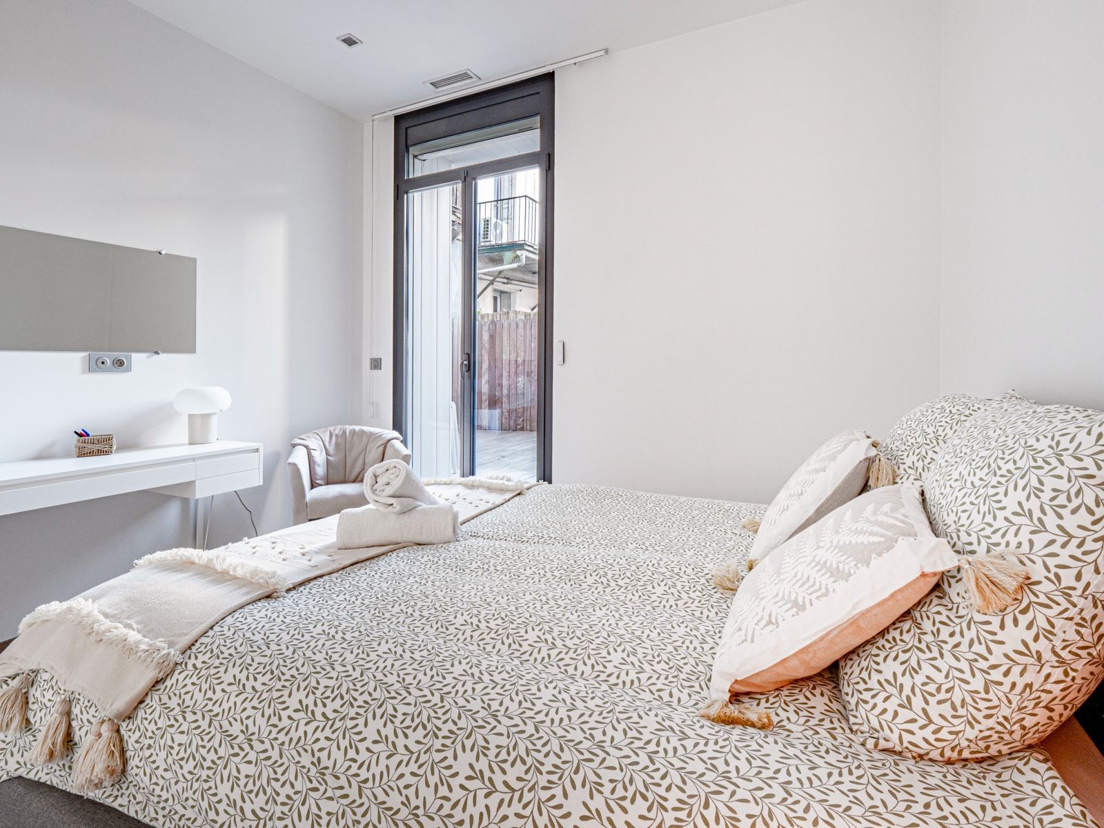 Un dormitorio con cama, una silla, un escritorio y una puerta que da a un área exterior.
