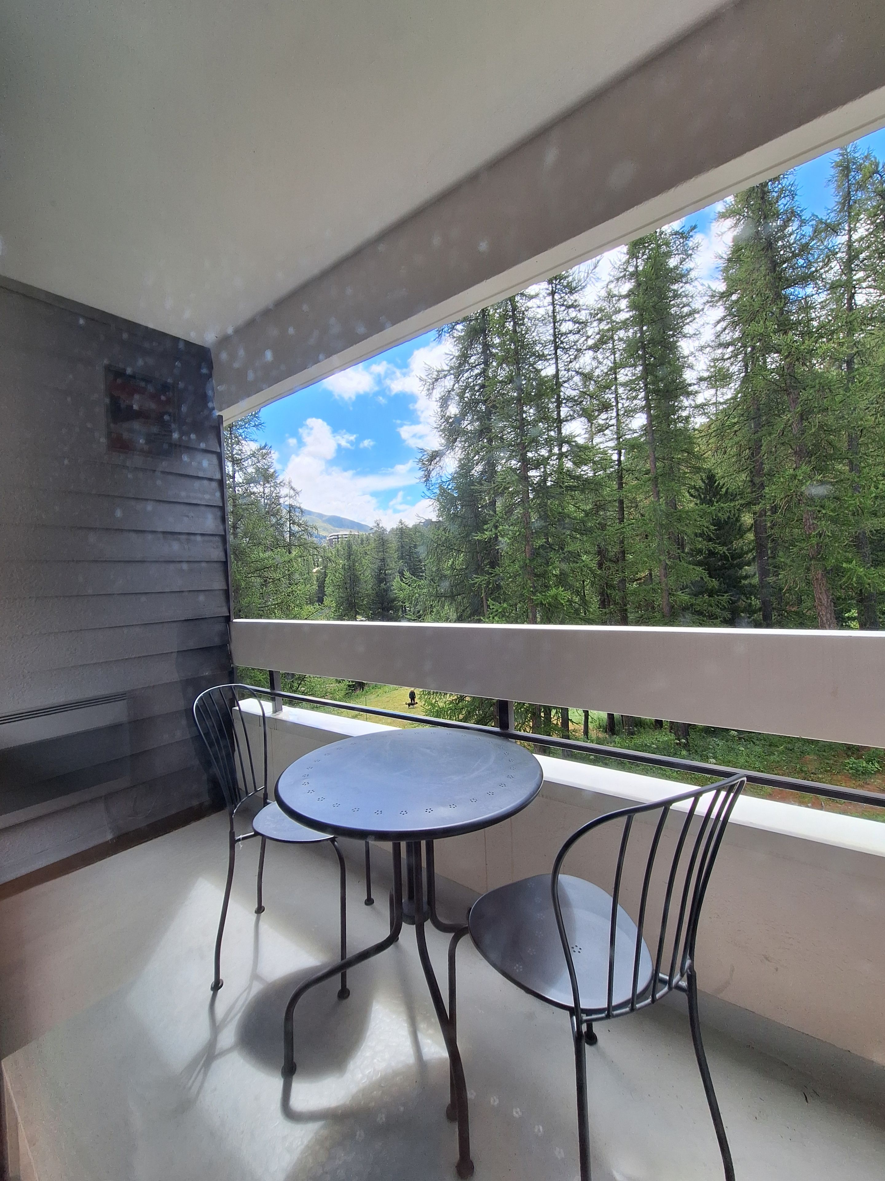 A balcony with a table and chairs, overlooking a forested area.