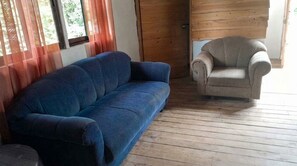 Una habitación con un sofá azul y un sillón color beige, suelo de madera y una puerta.