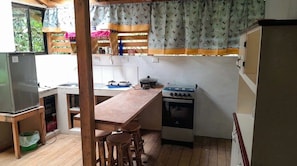 Una cocina compacta con una mesa de madera, taburetes de bar, cocina a gas y un refrigerador.