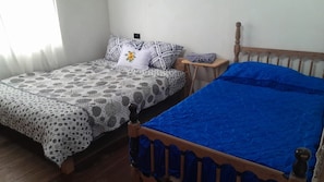 Dos camas individuales con ropa de cama diferente, una mesita de noche de madera pequeña y una ventana con cortinas.