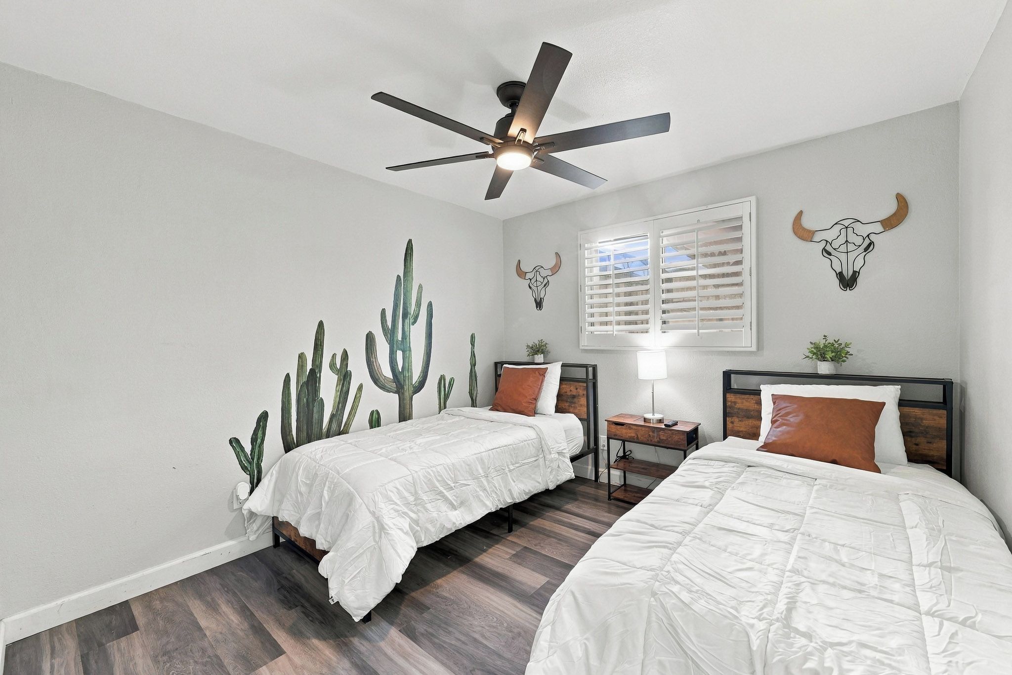 A bedroom with two beds, a ceiling fan, and wall art including a cactus mural and skulls.