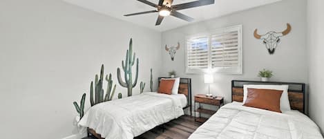 A bedroom with two beds, a ceiling fan, and wall art including a cactus mural and skulls.