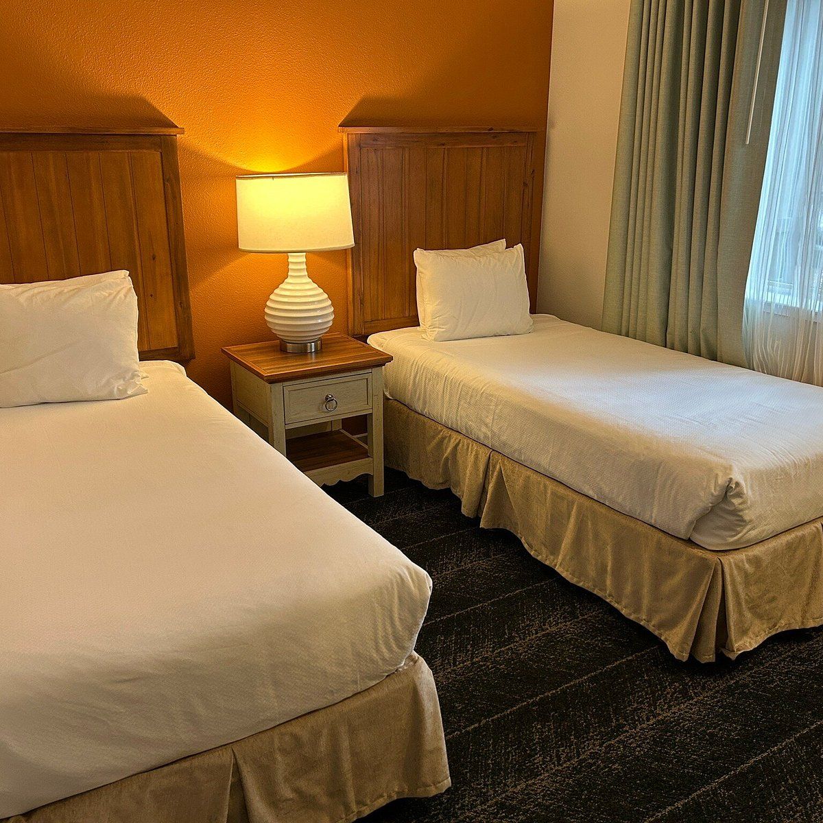 A hotel room with two beds, a nightstand with a lamp, and a window with curtains.
