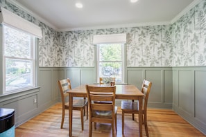Comedor con mesa y sillas de madera, una ventana con vista al exterior y papel tapiz estampado.