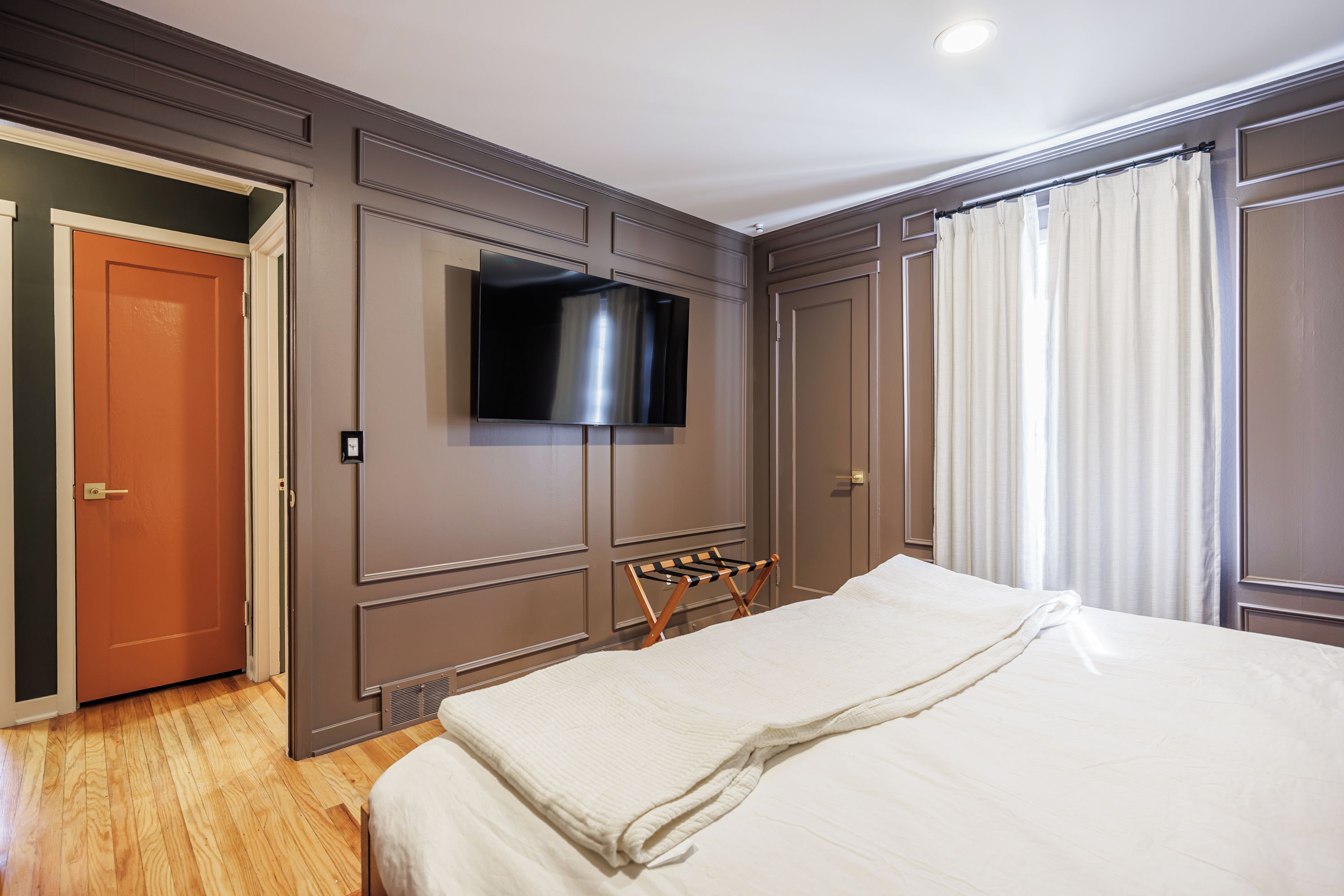 Habitación de hotel con cama, televisor montado en la pared, puerta y ventana con cortinas.