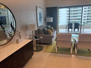 A modern living room with a sofa, a coffee table, and a dining area with chairs. - Garza Blanca Cancun: Luxury 1-Bedroom Suite w/ Ocean Views and AC (playa mujeres)
