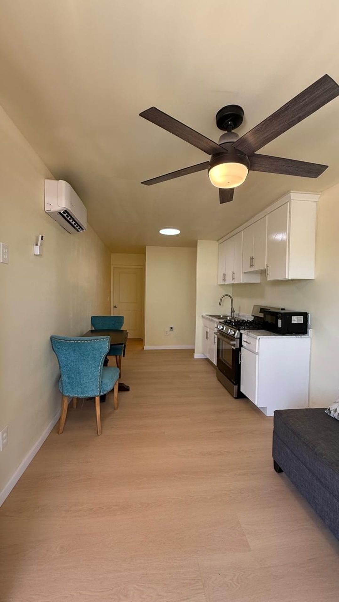 Une cuisine de taille réduite avec des meubles blancs, une cuisinière et un ventilateur de plafond.