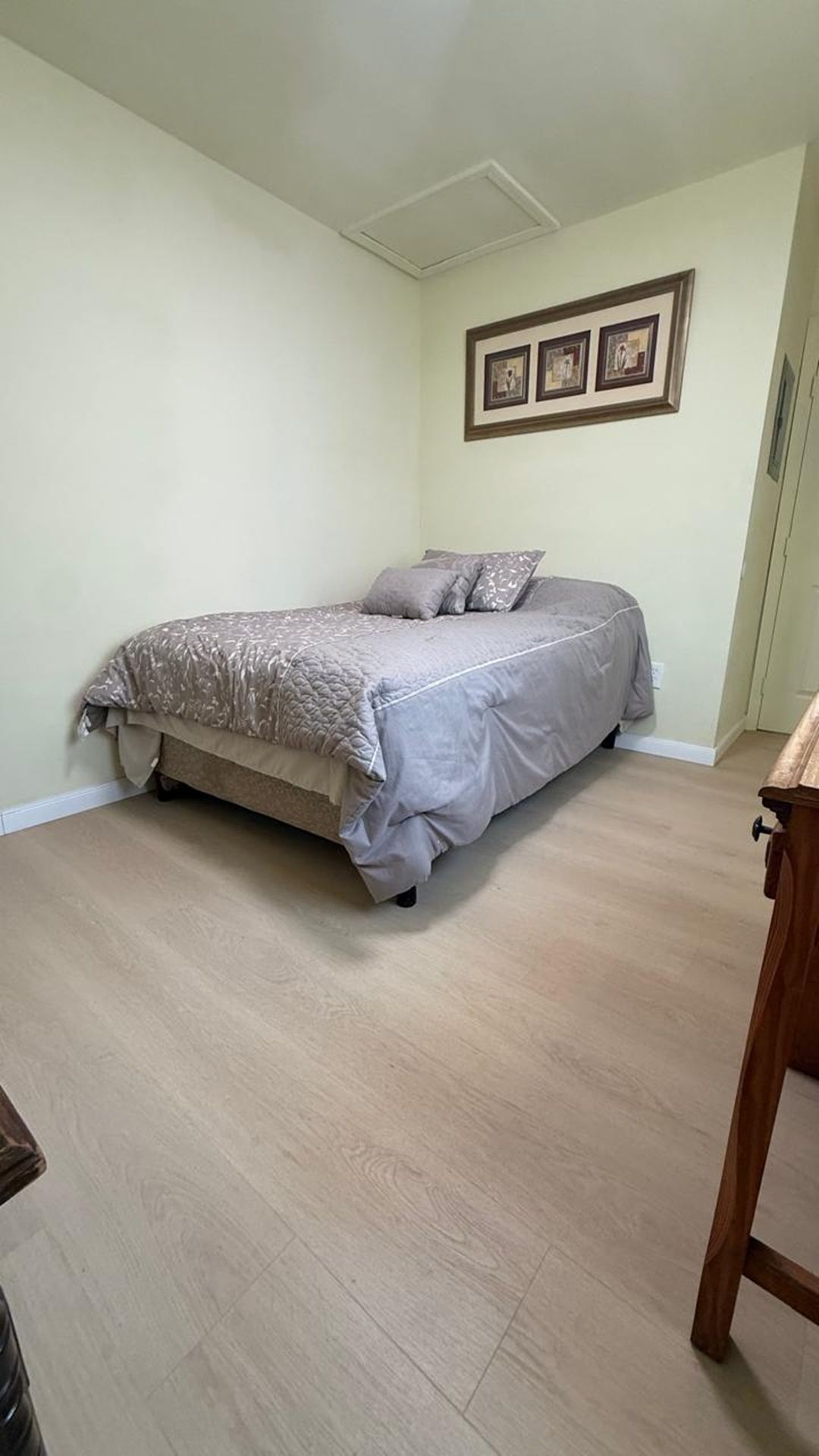 Une chambre à coucher avec un lit, une table de chevet en bois et un tableau encadré accroché au mur.