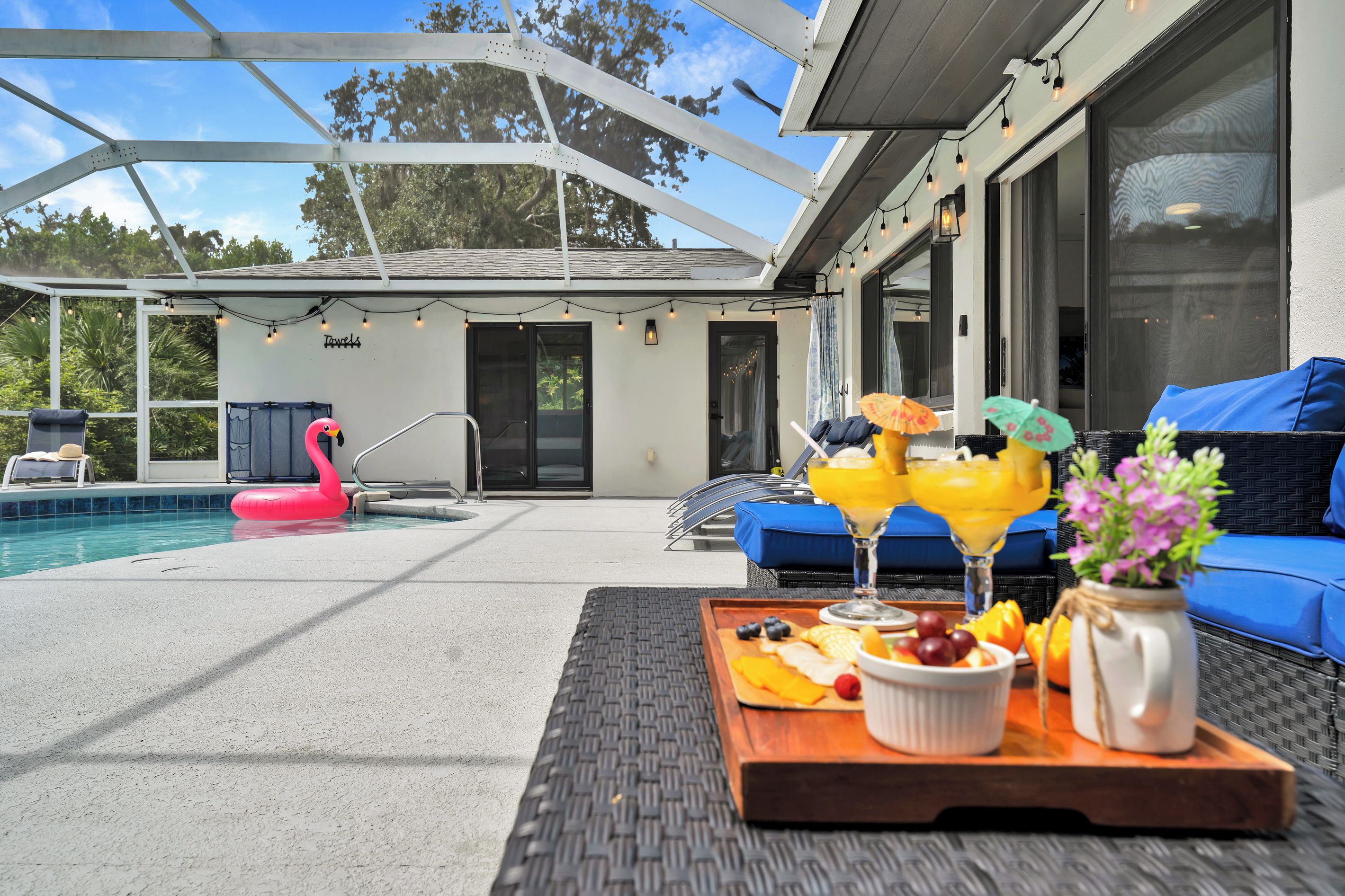 A poolside area with a lounge chair, a dining table with food and drinks, and a pink flamingo float.