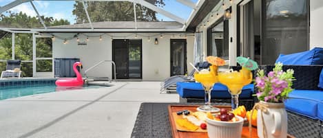 A poolside area with a lounge chair, a dining table with food and drinks, and a pink flamingo float.