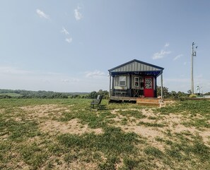Et lille, etetages hus med en rødlakeret dør og en veranda, omgivet af en græsmark.