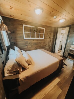 Quarto com painéis de madeira, uma cama grande, uma janela com cortinas e uma porta.